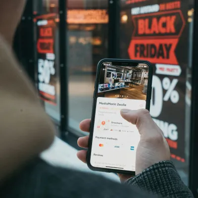 Person holding smartphone displaying MediaMarkt Zwolle app with Black Friday sale signs in background