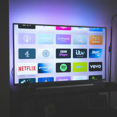 Smart TV screen displaying streaming apps like Netflix, Prime Video, Spotify, and BBC iPlayer in a dimly lit room.