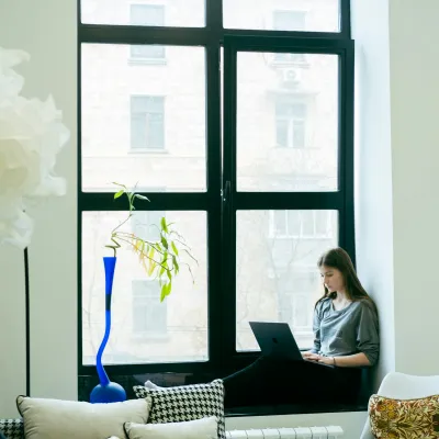 a woman sitting on a couch with a laptop in front of a window