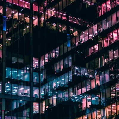 Night view of a modern office building with colorful illuminated windows and reflections on glass facade.