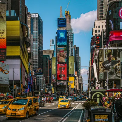 Busy New York City street with yellow taxis, skyscrapers, and vibrant digital billboards on a clear day