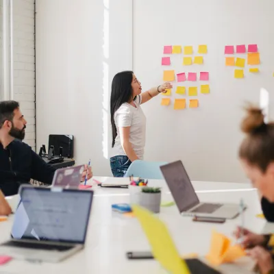 Team collaborating in a bright office with sticky notes on the wall and laptops open around a white table.