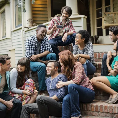 Group of young adults socializing and laughing together on a house porch steps on a sunny day