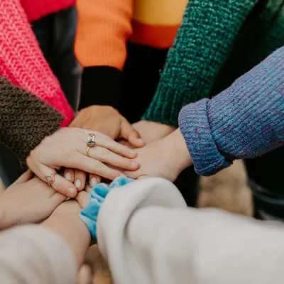 Group of people putting hands together in a show of unity and teamwork with colorful sweaters.