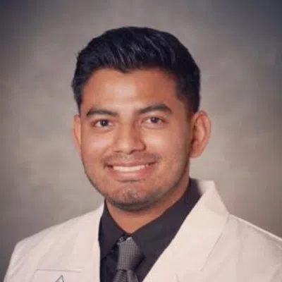 Smiling man wearing a white medical coat with name R. Duran and a medical emblem on the chest pocket.