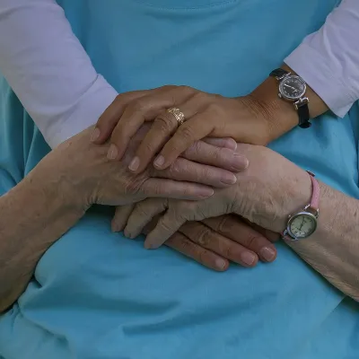 Close-up of two people wearing blue clothing, showing supportive hands clasped gently together.