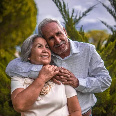 Elderly couple embracing outdoors with greenery, smiling and showing affection and happiness together.