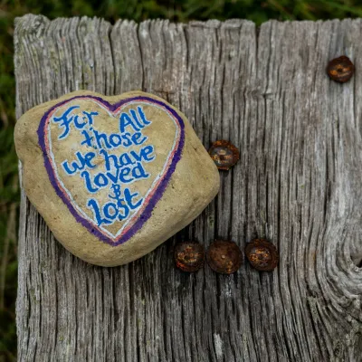 Heart-painted rock with message for loved and lost placed on weathered wooden surface outdoors.