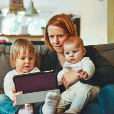 Mother with two young children sitting on a couch using a tablet in a cozy home setting.