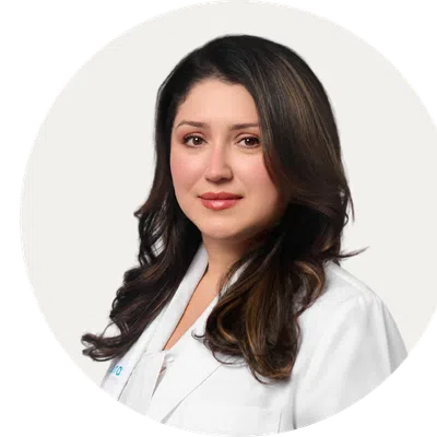 Professional woman with long dark hair wearing a white lab coat against a light background.