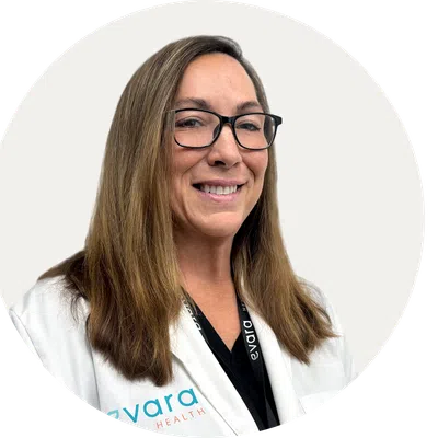 Smiling female healthcare professional wearing glasses and white coat with Evara Health logo on it