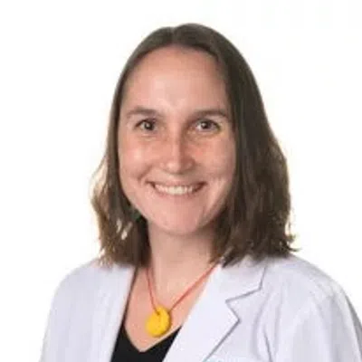 Smiling woman in white lab coat with Evard Health logo and yellow necklace on white background