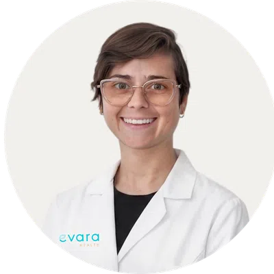 Smiling healthcare professional wearing glasses and a white lab coat with Evara Health logo on plain white background.