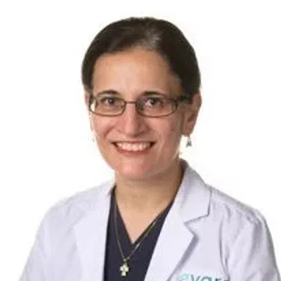 Smiling female doctor wearing glasses and a white lab coat with Evora Health logo on the chest.