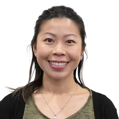 Smiling Asian woman with long hair wearing a green top and black cardigan against white background