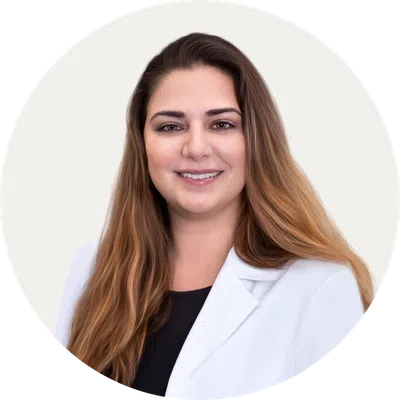 Professional woman with long brown hair wearing a white blazer and black top, smiling against a white background.
