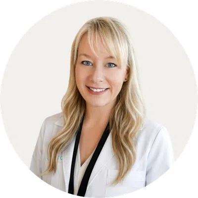 Smiling female doctor with blonde hair wearing white coat and black lanyard on light background