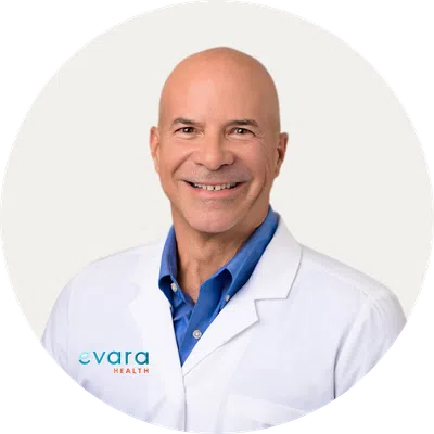Smiling bald male doctor in white coat with blue shirt against white background