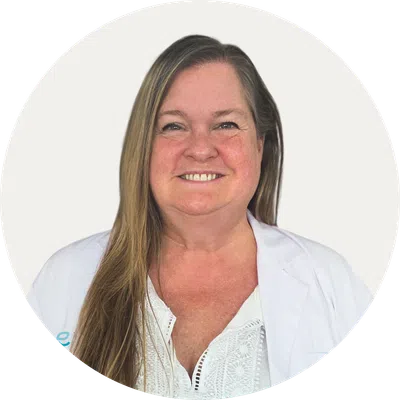 Smiling woman with long hair wearing a white lab coat and white blouse against a plain background