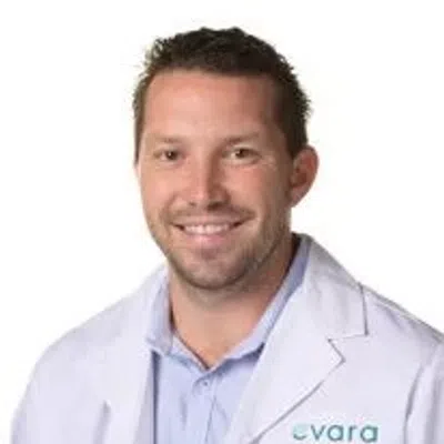 Smiling male healthcare professional wearing a white lab coat with Evara Health logo on chest.