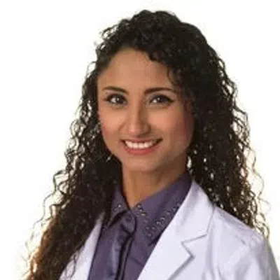 Smiling female healthcare professional with curly hair in a white lab coat over purple shirt