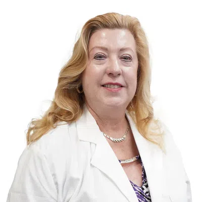 Smiling middle-aged woman with blonde hair wearing a white lab coat and patterned blouse on white background