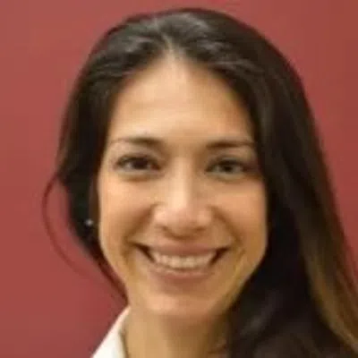 Smiling woman with long dark hair against a solid red background, appearing friendly and approachable.