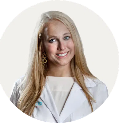 Smiling blonde female doctor wearing white coat and stylish earrings against a plain background