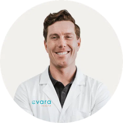Smiling male healthcare professional wearing white lab coat with Evara Health logo on a white background.