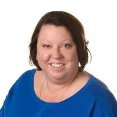 Smiling woman with short brown hair wearing a bright blue top against a white background