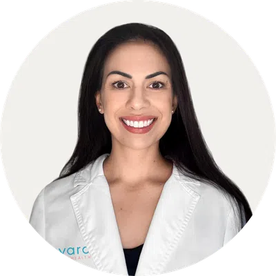 Smiling woman with long dark hair wearing a white lab coat against a plain light background