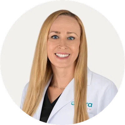 Smiling female healthcare professional with long blonde hair wearing a white lab coat on white background