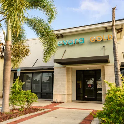 Exterior view of Evara Gold store with palm trees and shrubs under blue sky