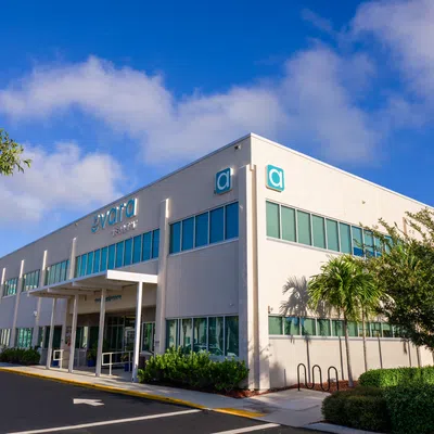 Modern two-story commercial building with large windows under a blue sky and landscaped greenery around.