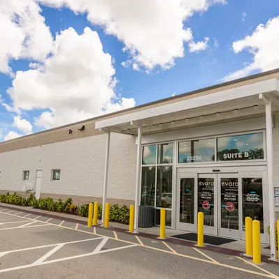 Exterior view of a modern commercial building entrance labeled Suite B with yellow bollards and a blue sky.