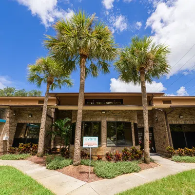 Single-story brick commercial building with palm trees, blue sky, and landscaped front garden under bright sunlight