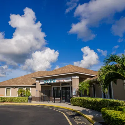 Community center building under a bright blue sky with palm trees and neatly trimmed hedges around the entrance.