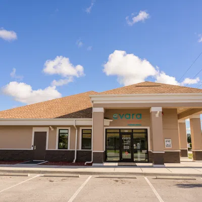 Evara medical clinic building with beige exterior under blue sky with scattered clouds and empty parking lot.