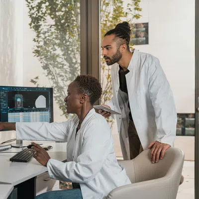 Two doctors analyzing brain scans on computer monitors in a modern medical office with large windows.