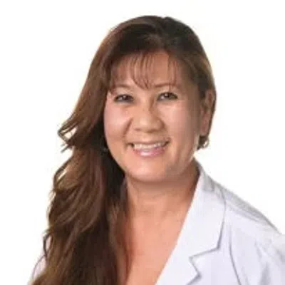 Smiling female healthcare professional with long brown hair wearing a white lab coat against white background.