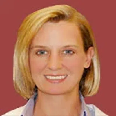 Portrait of a smiling woman with short blonde hair against a solid maroon background.