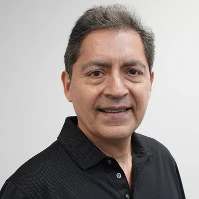 Smiling middle-aged man with short salt-and-pepper hair wearing a black polo shirt against a plain background