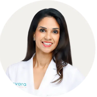 Smiling female doctor with long dark hair wearing a white medical coat against a white background