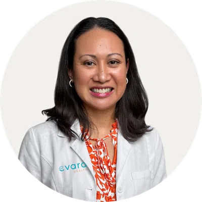 Smiling female healthcare professional wearing a white coat and orange floral blouse against a white background