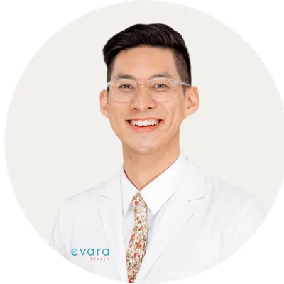 Smiling male healthcare professional wearing glasses and white coat with floral tie on white background.