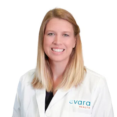 Smiling female healthcare professional wearing a white Evara Health lab coat on a white background