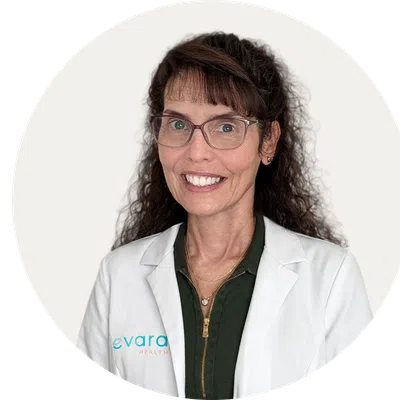 Smiling woman in white medical coat wearing glasses with curly hair over a white background.