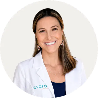 Smiling woman in a white medical coat with Evara Health logo on a white background.