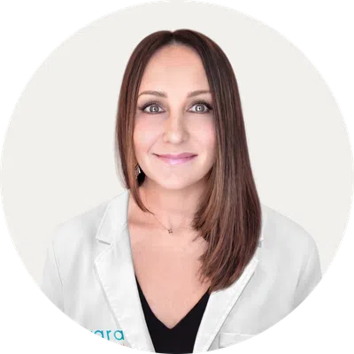 Female healthcare professional in white lab coat with Evara Health logo and clear glasses smiling at camera
