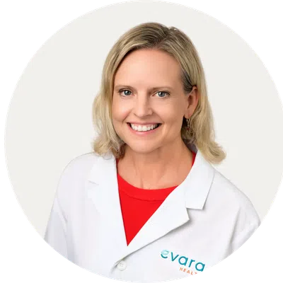 Smiling woman wearing a white Evara Health lab coat with a red shirt and geometric background